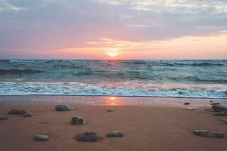 Scenic view of beautiful sunrise above the sea. Stones on the sand on the beach in the morning light rising from the seaIndia, Goa, Kerala, Asia, Indian ocean.の写真素材