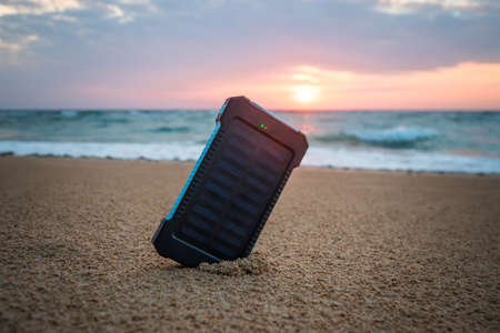 Portable Small Solar Panel near the Atlantic Ocean. Powerbank for charging mobile phones and other devices via USB. Solar battery under the sun on the background of beautiful dawn and cloudy sky.の写真素材