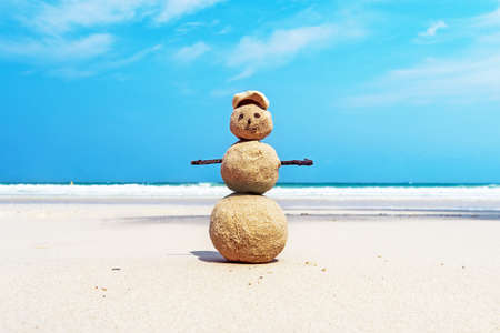 Christmas positive Sandy Snowman in red Santa Claus hat at ocean sunset beach. New Year vacation discounts in hot countries destinations conceptの写真素材