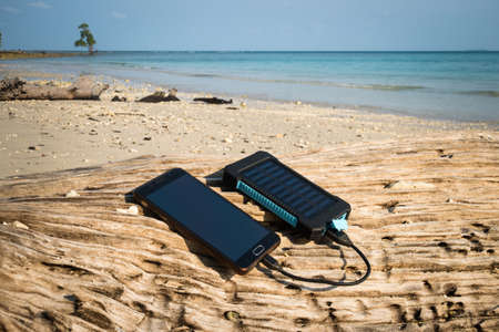 Alternative energy source. battery is charged by solar energy. Charging mobile devices in the wild. island beach.の写真素材
