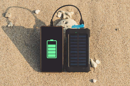Portable solar panel is on the beach in the sand and charges the battery of the frameless mobile phone. use of solar energy in the wild on a desert islandの写真素材