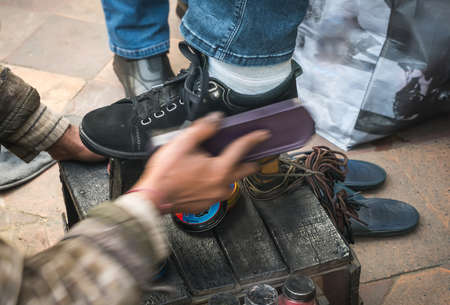 Indian man cleaning customer shoes on city pavement. new Delhi India. Brushing brush your black shoes with black cream.の写真素材