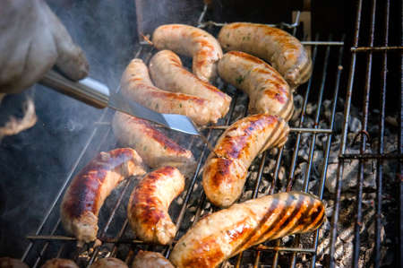 Fresh sausage. Hot dogs grilling outdoors on a gas barbecue grill. Male cook flips grilled sausages on open fire.の写真素材