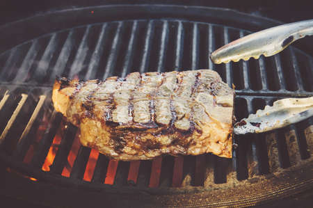Beef steaks on the grill with flames. The chef flips a piece of meat beef on the grill with open fire.の写真素材