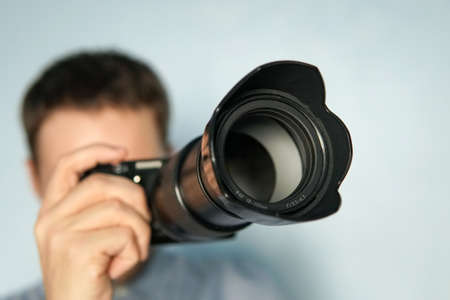 Young photographer on blue background. Mirrorless camera close up in the hand of a young man on blue...