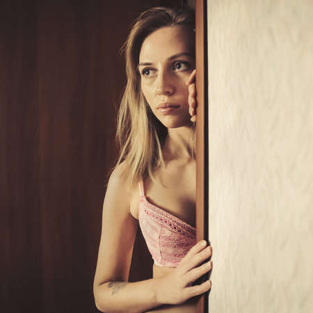 Portrait of young Caucasian Blond Woman Looking Out of the Doorway with Face Half Lit and Partially in Shadow. Vertical Imageの写真素材