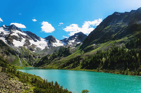 Clear blue river in mountains. Quiet river flowing in between the mountains on the background of snowy peaks of the high mountainsの写真素材