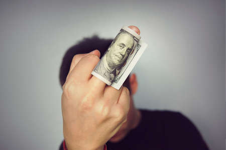 sign middle finger money hundred dollars bill man in a black t-shirt neutral grey background.の写真素材