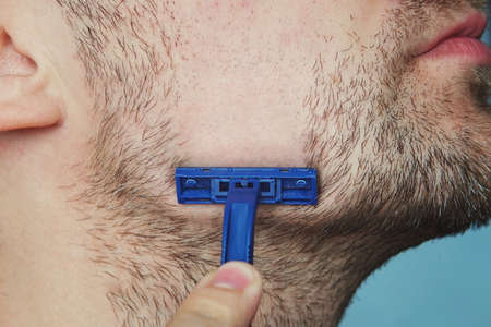 view of a young bearded man with a brutal razor. face on the blue background.の写真素材