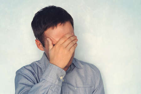 a young guy in a blue shirt is holding his head. the concept of fatigue.の写真素材