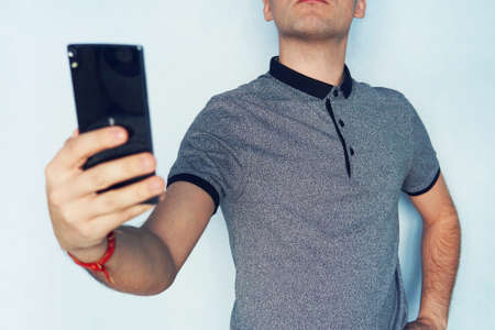 guy takes himself on a mobile phone. A young man takes a selfie. a man reading SMS on a black smartphone. A person looks into the phone screen on blue backgroundの写真素材