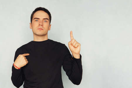 Attractive young man in white t-shirt pointing right with his finger on blue background.の写真素材