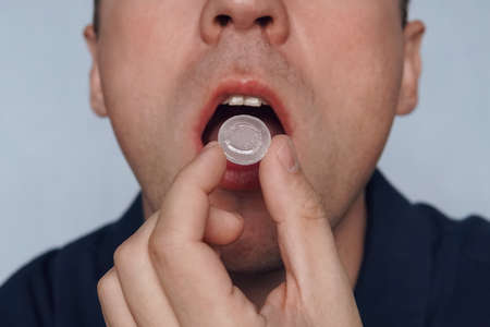 young man puts in his mouth a sucking pill for sore throat. Self-medication for flu and cold. Sick with a sore throat, mint for fresh breath. close upの写真素材