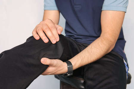 athlete suffering from knee pain. young man is holding his hands over his sick knee on a blue background. patella fracture.の写真素材