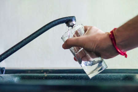 Closeup shot of a man pouring a glass of raw unfiltered drinking water from a kitchen tap. a man...