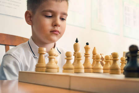 Child playing chess, on white background. young man looks at the chess pieces.の写真素材