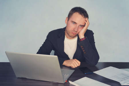 Portrait of tired male feeling headache while working with notebook computer at table. Fatigue during labor with technology concept. tired at work. workaholismの写真素材