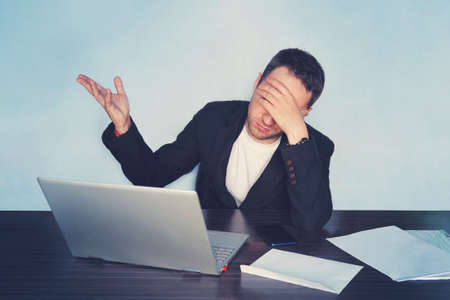 bankruptcy of the enterprise. Business man working at a computer in the office holding his head with his hand and closes his eyes.の写真素材