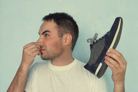 A man pinches his nostrils closed over the odor given off from the athletic shoe he is holding.の写真素材