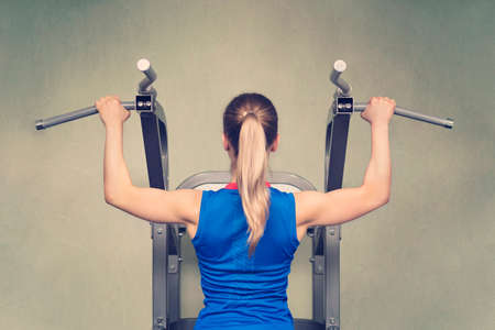 Sexy fit woman performing pull ups in a bar. Hard training. Rear view. blonde in a blue t-shirt is...