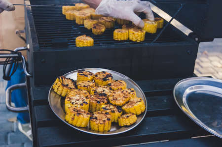 The process of preparation of grilled vegetables. Tasty grilled corns on the grill pan and metal plate. Chef's hands white gloves.の写真素材