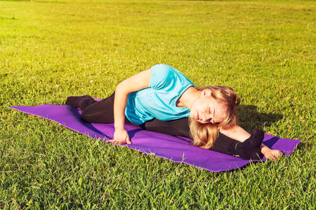 blonde woman coach in a sporty short top and gym leggings makes a wide twine on the rug for yoga...