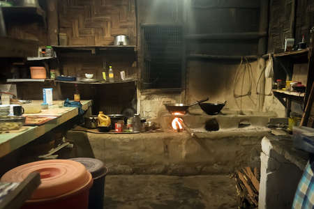 Traditional kitchen in old Nepali house in small remote village in Himalayas with open fire place, smoking coal, kettles, frying pans and pots. Interior of a poor asian house.の写真素材