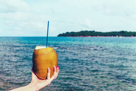 Woman s hands holding coconut on tropical beach against the blue seaの写真素材
