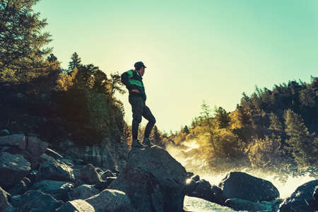 joyful man travel mountains. Picturesque location in Europe. Mountains and sea view. Young traveler guy standing on a stone on the background of water splashesの写真素材