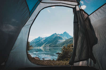 View from tent entrance on beautiful lake in the morning. Camping in the mountains. Beautiful view from the tent. Rest in the wild. Atmospheric toned photo.の写真素材