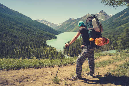 Photo from back of tourist man with walking sticks with his hands up on mountain hill near lake. tourist holding sticks for Nordic walkingの写真素材