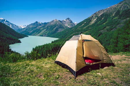 Tourism and traveling concept. Beautiful summer landscape with mountains and tourist tent. Yellow tent stands near the lake in the mountains, Bright Sunny day in the mountains.の写真素材