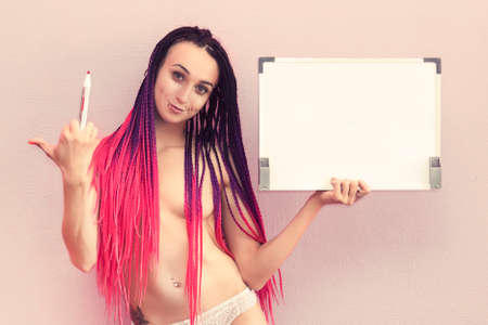 Wear something a little sexy Young well-graced attractive girl wearing stylish lingerie and sitting on the floor, while holding empty blank board on the pink backgroundの写真素材