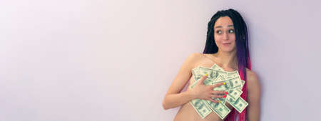 Young pink hair girl holding money. Portrait on pink background. copy space. copyspace. a young happy girl covers her Breasts with banknotes of one hundred dollars.の写真素材