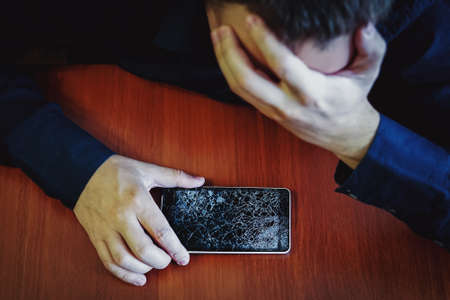 Handsome angry businessman showing broken smartphone with crashed screen. Isolated on white...