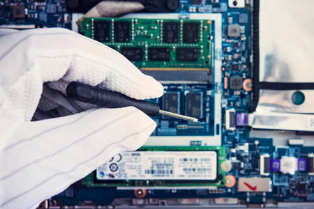 Replacement of memory in the laptop, in one of the service centers for repair of laptops. hand in a white glove holds a screwdriver on the background of disassembled modern ultrabook.の写真素材
