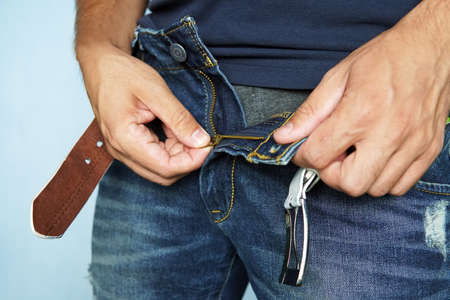 Close-up Of A Man's Hand Unzipping The Blue Jeans. unbuttoned blue pants