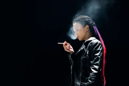 Beautiful woman Smoking a cigarette on a black background in the night light. concept of Smoking and harmful lifestyle. nicotine addiction, dependenceの写真素材