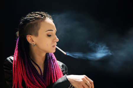 Fashion art portrait of beauty model woman in bright lights with smoke. Smoking girl, Close up of a female inhaling from an electronic cigarette. Night life concept. bad habit, harmful habit.の写真素材