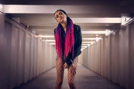 Young fashion woman in modern tunnel. Model of non-standard appearance with extreme style. Piercing on the face and African braids on hairstyles of different colors. subcultureの写真素材