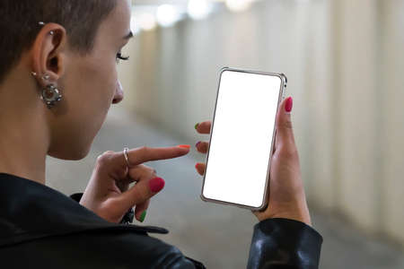 Girl holding on smartphone with empty blank screen monitor on the background bokeh light in street atmosphere, freelancer hipster using in female hands smart phone with blank template, blurの写真素材