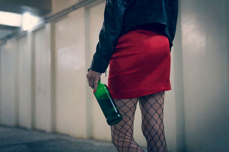 Drunk young woman walking down the hall smoke cigarettes. Girl is holding a bootle of wine at the level of the sexy thighs in pantyhose. Romantic date. Girl hobbles stumbling. Drunken gait.の写真素材