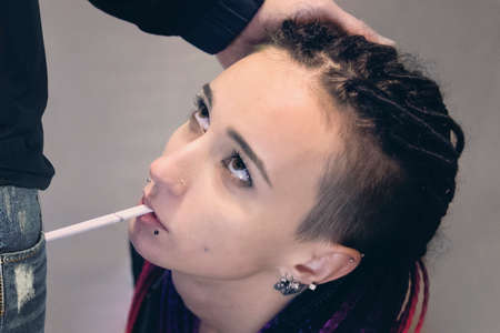 Smoking young pretty girl kneeling in front of an adult man. metaphor of Smoking as a dependence....