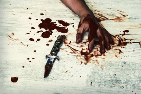 Conceptual image of a victim hand holding a sharp knife with blood on it resting on a white vintage floor. Concept photo of murder and crimeの写真素材