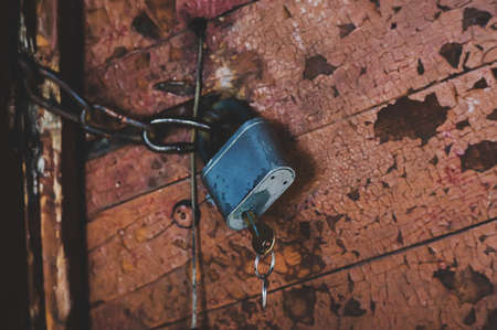 Lock on the door of an old wood house, village style. the key into the old metal lock on the background of the Stroy doors in shabby paint. Locked door. The castle in chains.の写真素材