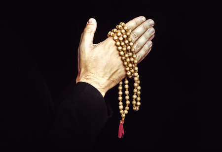 Hands folded in prayer on a black isolated background. The priest in prayer. Rosary in the hands of...