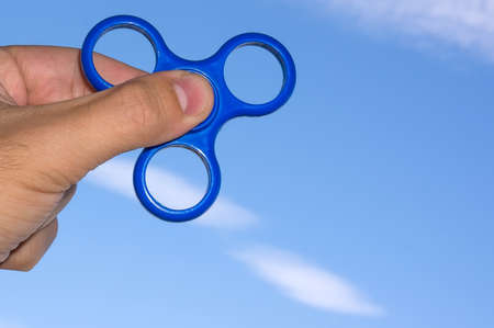 Hand holding popular fidget spinner toy on sky background with copy space.の写真素材