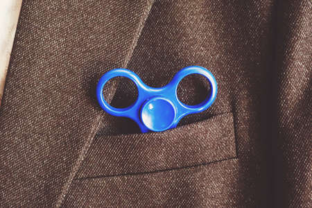 Blue spinner in the pocket of the blazer business businessman. Antistress toy for nervous. Powerful spinner, Twister for hands entertainment rotating toy.の写真素材