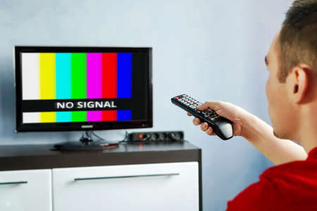 Remote control in hand in front of TV. Couch potato. No signal screen banner.の写真素材