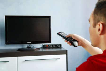 Men with the remote control, front of the television. Young guy switches channels on the remote from the TV. Turning the TV on or offの写真素材